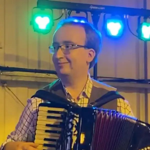 Alan Brunier smiling with an accordion and bright lights behind him