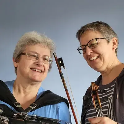 A photo of Ali and Linda, who are smiling while holding their musical instruments.