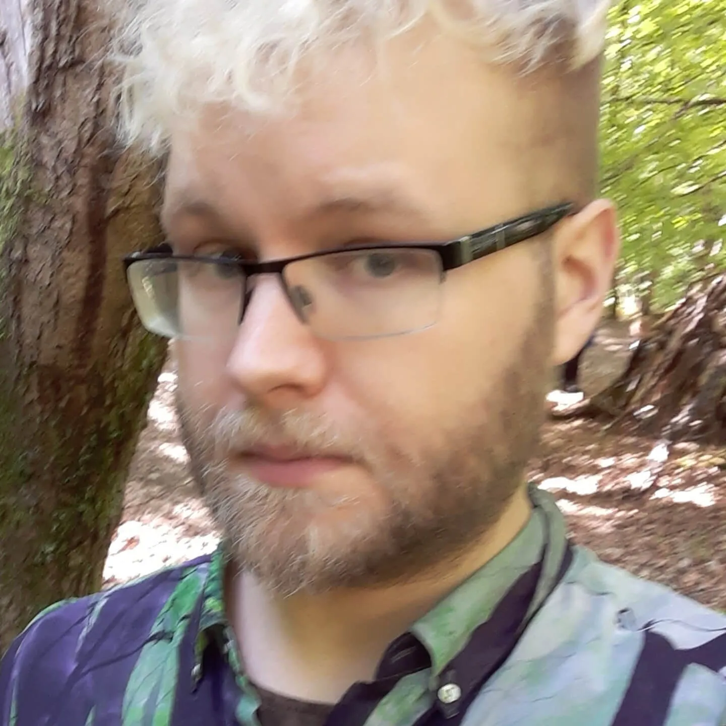 Sam, a person with glasses and a short blond beard, in the woods