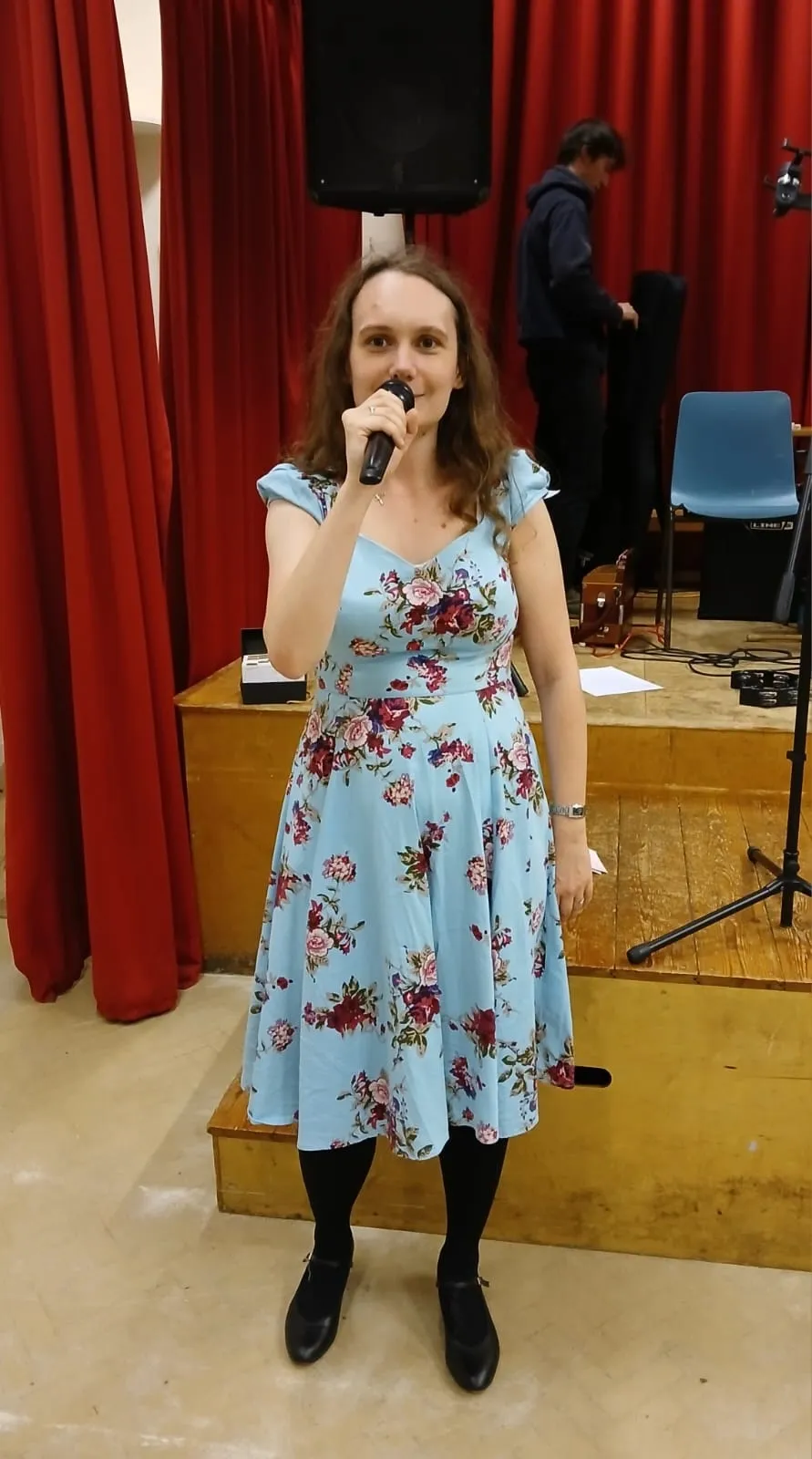 Lauren is a woman in a dress, and is holding a microphone.