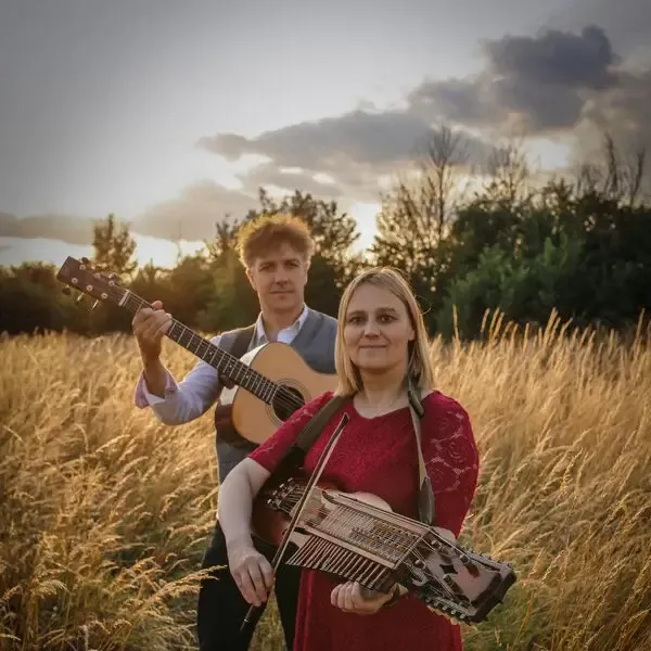 Vicki & Jonny in a field at harvest time with a guitar and a nyckelharpa