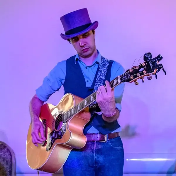 Adam Rich-Griffin, wearing a purple top hat and playing a guitar